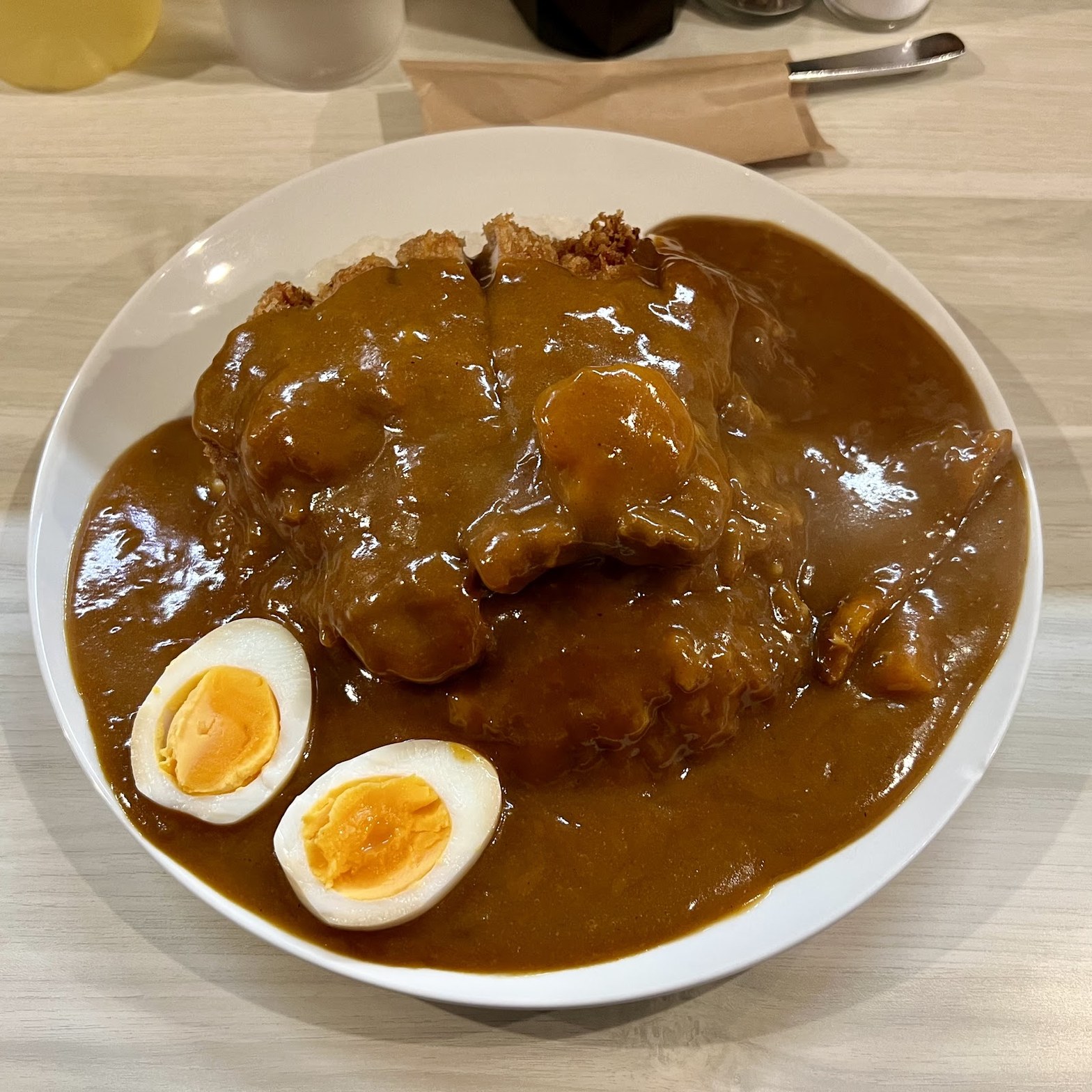 茶色いカレーソースがたっぷりかかった揚げ物と半熟卵2個が盛られた白い大皿